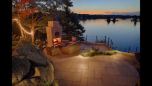 Outdoor stone fireplace by a lake at night from Green Up Landscaping